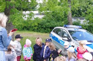 policjantka rozmawia z dziećmi w tle zieleni i placu zabaw terenu przedszkola