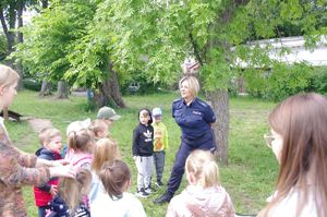 policjantka rozmawia z dziećmi w tle zieleni i placu zabaw terenu przedszkola
