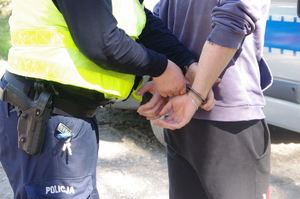 policjant i sprawca z kajdankami na dłoniach w tle radiowóz