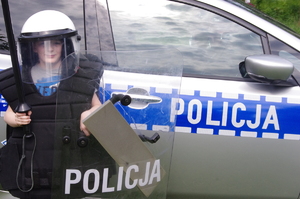 dziecko przebrane w strój do zadań specjalnych Policji w tle radiowóz