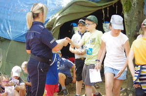 policjantka wręcza ulotki w tle las i uczestnicy obozu