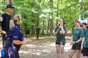 policjantka wręcza ulotki w tle las i uczestnicy obozu