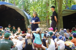 służby rozmawiają z uczestnikami obozu w tle las i namioty