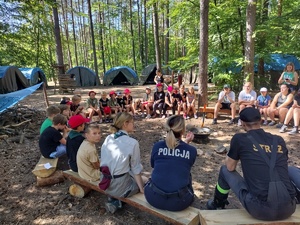 policjanci i strażacy na spotkaniu z harcerzami w tle las i namioty
