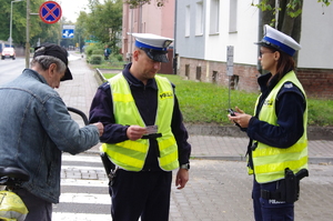 policjanci rozmawiają z rowerzystami w tle ulica i zabudowania