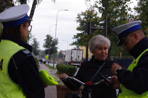 policjanci rozmawiają z rowerzystami w tle ulica i zabudowania