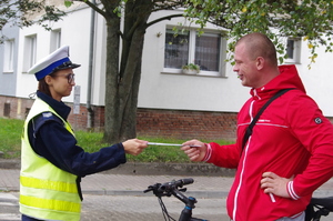 policjanci rozmawiają z rowerzystami w tle ulica i zabudowania