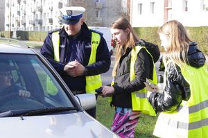 policjanci i uczniowie rozmawiają z kierowcami w tle ulica i zabudowania