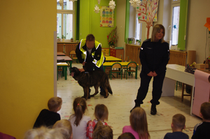 policjanci z psem policyjnym rozmawiają z dziećmi w tle sala w przedszkolu