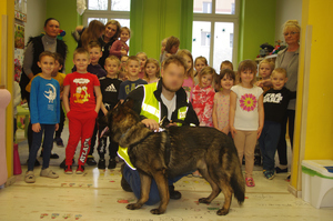 policjanci z psem policyjnym rozmawiają z dziećmi w tle sala w przedszkolu