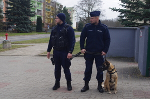 policjanci patrolują ulice z psem służbowym w tle zieleń i zabudowania
