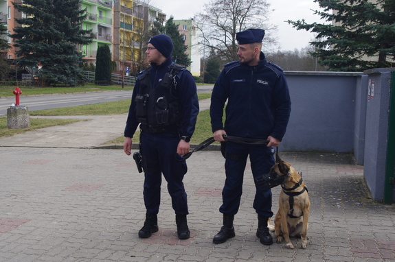 policjanci patrolują ulice z psem służbowym w tle zieleń i zabudowania
