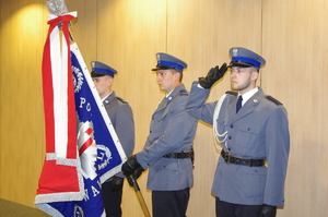 policjanci umundurowani przy sztandarze w tle ściana