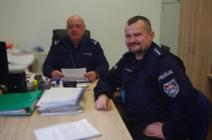 policjanci umundurowani za biurkiem w tle pomieszczenie służbowe