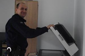 policjant przy drukarce w tle ściana