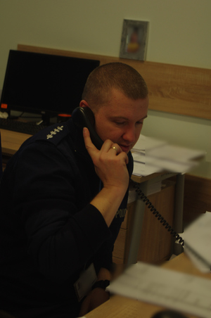 policjant rozmawia przez telefon   w tle ściana