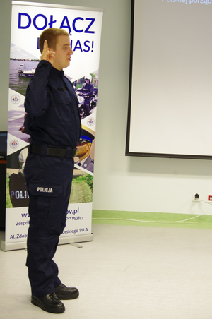 policjant skalda ślubowanie w tle pomieszczenie i baner promujący zawód policjanta
