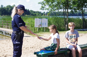 policjanci na plaży rozmawiają z dziećmi  w tle jezioro