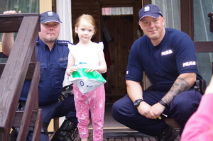 wspólne zdjęcie policjantów i dziewczynki w tle domek Brda