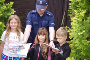 policjant wręcza dzieciom niespodzianki w tle drewniany dom