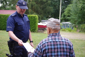 Policjant wręcza ulotkę mężczyźnie w tle zarośla