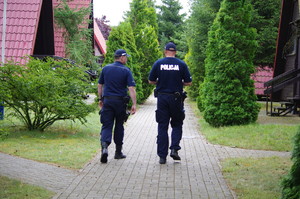 Policjanci idą kamienistą drogą  tle domki i zieleń