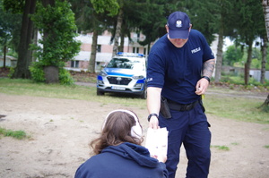 Policjant wręcza ulotkę kobiecie w tle radiowóz