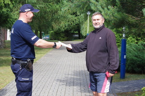 Policjant wręcza ulotkę mężczyźnie w tle zarośla