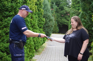 Policjant wręcza ulotkę kobiecie  w tle zarośla