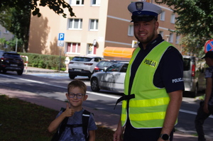 policjant z chłopcem w tle zabudowania i jezdnia