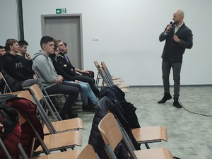 policjant w cywilnym ubraniu prowadzi spotkanie w tle sala i ekran a na nim film