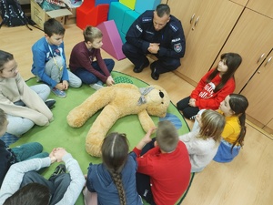 uczniowie ćwiczą pierwszą pomoc z policjantem w tle sala lekcyjna