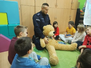 uczniowie ćwiczą pierwszą pomoc z policjantem w tle sala lekcyjna