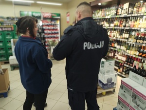 policjant ze sprzedawczynią przy regale z alkoholem w tle alkohole na półkach