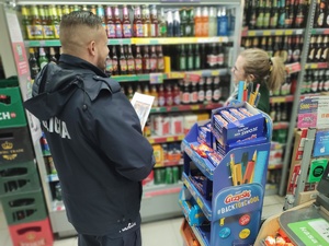 policjant ze sprzedawczynią przy regale z alkoholem w tle alkohole na półkach