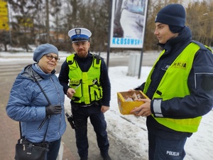 policjanci wręczają seniorom odblaskowe opaski i częstują ciastkami