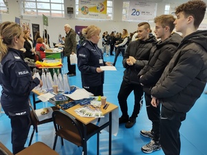 policjantki rozmawiają z odwiedzającymi targi  w tle wnętrze hali sportowej i inni wystawcy