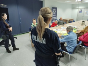 policjantki rozmawiają z seniorami  w tle sala, stoły i seniorzy