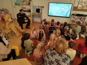 dzieci wspólnie z policjantem oglądają bajkę w tle ekran i bajka