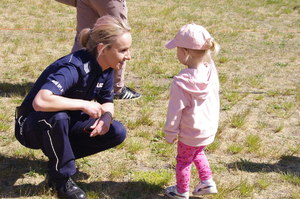 policjantka kuca przy małej dziewczynce w tle boisko
