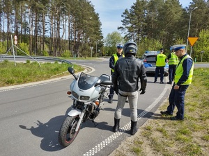 policjanci kontrolują motocyklistę w tle radiowóz i policjanci