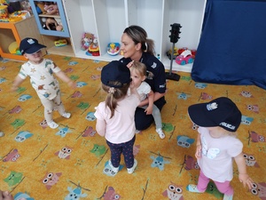 maluchy w policyjnych czapkach w tle policjantka trzyma dziecko na kolanach
