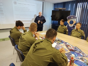 Komendant rozmawia z uczniami w tle ekran i sala
