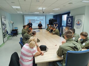 policjantka rozmawia z uczniami w tle ekran i sala