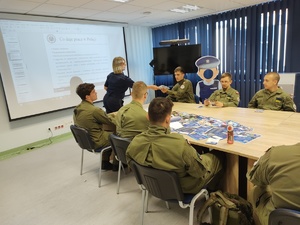 Policjantka rozmawia z uczniami w tle ekran i sala
