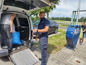 zbiórka nakrętek przed budynkiem komendy w tle policjanci i cywile, zaparkowane auta
