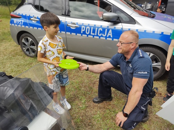policjant rozmawia z dziećmi w tle radiowóz i zieleń
