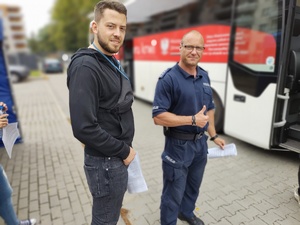 mężczyźni w tym policjant przed ambulansem, w tle zabudowania