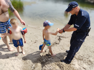 policjant rozmawia z plażowiczami w tle plaża