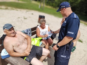 policjant rozmawia z plażowiczami w tle plaża